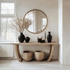 a table with vases and candles on it in front of a round mirror above