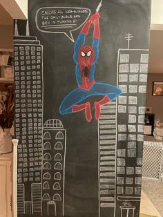 a chalkboard drawing of a spiderman hanging from a building with buildings in the background