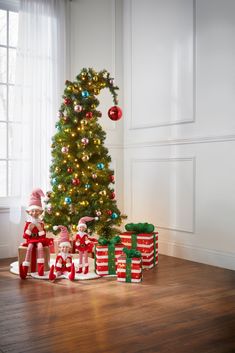 a christmas tree with presents under it in front of a window and other decorations on the floor