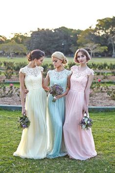 three bridesmaids in pastel gowns standing next to each other on the grass