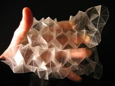 a hand holding an object made out of white origami pieces on a black background