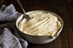 a spoon in a bowl filled with cream on top of a wooden table next to a napkin