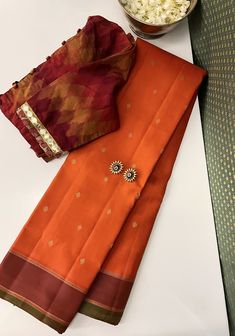 Oranges in kanchipuram silk are effortlessly sacrosanct. This pure handwoven kanchipuram silk has varying shades of oranges throughout. The body is a bright orange with simple zari woven buttis, while the pallu and border are a deeper burnt orange. The border has a green selvedge that adequately highlights the oranges and the pallu has pure zari woven stripes through it all. With numerous styling options, this saree effortlessly transitions from intimate family gatherings to grand weddings. Burnt Orange Saree, Orange Saree Contrast Blouse, Orange Kanchipuram Saree, Pearl Blouse, Bridal Lehenga Designs, Orange Saree