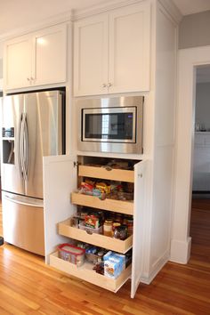 a kitchen with white cabinets and wooden flooring has an open pantry in the middle