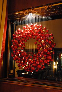 a christmas wreath hanging from the side of a mirror in front of a window with red ornaments on it