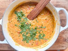 a wooden spoon in a pot filled with red lentils and garnishes