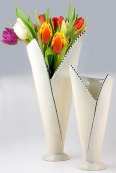 two white vases with tulips and other flowers in them on a table