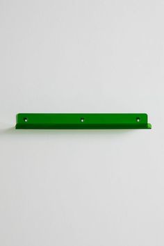 a green shelf with three holes in the middle on a white wall behind it is an object that appears to be part of a piece of furniture ornament