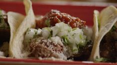 three tacos with meat and vegetables in them on a red plate, ready to be eaten