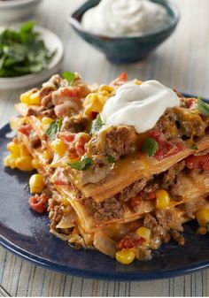 a blue plate topped with lasagna covered in ground beef and vegetables next to sour cream