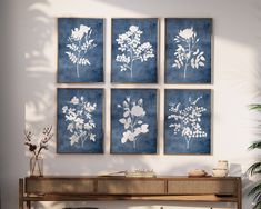 four blue and white floral prints on a wall above a wooden table in front of a potted plant