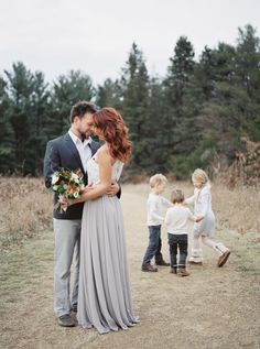 a man and woman are hugging in the middle of a field with two children behind them