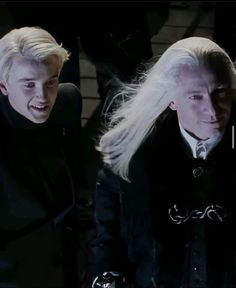 two men with long white hair and black clothing, one is wearing a suit while the other wears a tie