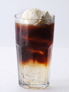 an ice cream sundae in a tall glass on a white table with brown liquid