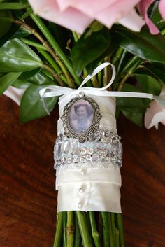 a bouquet of pink roses with a photo on the ribbon and an ornament attached to it