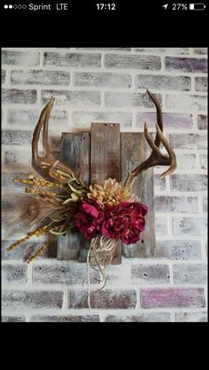 a deer's head mounted on a brick wall with flowers and antlers attached to it