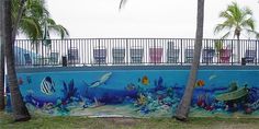 a mural on the side of a swimming pool with fish and corals painted on it