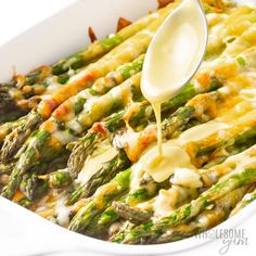 a spoon is being drizzled over asparagus in a casserole dish