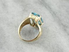 This vintage gold mounting is simple with decorative, sweeping shoulders on the sides and secure prongs. We've set this piece with a modern, large blue topaz. The color of this stone is deeper, a rich, almost turquoise color. This would make a lovely cocktail ring, and is also a sturdy enough stone to wear everyday! Metal: 10K Yellow Gold Gem: Blue Topaz 9.81 Carats Gem Measurements: 14 x 10.5 mm, Rectangle Emerald Cut Ring Size: 7.50 Marks: "10 K MAR" Stamped on the inside band Classic Blue Topaz Ring With Tension Setting, Modern Topaz Ring With Polished Finish, Blue Square Cut Topaz Ring, Modern Emerald-cut Blue Topaz Jewelry, Square Cut Blue Topaz Jewelry, Square-cut Blue Topaz Gemstone Jewelry, Rectangle Ring, Bypass Ring, Emerald Cut Rings