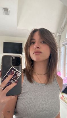 a woman taking a selfie with her cell phone in front of her face while wearing a gray tank top