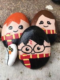 three painted rocks sitting on top of a stone covered in paper mache characters, one with glasses and the other with harry potter's hair