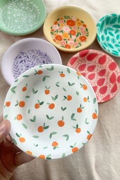 a hand holding a small bowl in front of five bowls with different designs on them