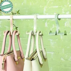 three purses hanging on a rack in front of a green wall