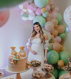 a pregnant woman standing in front of a cake and desserts at a baby shower