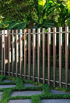 a wooden fence surrounded by green plants and stone walkways in the middle of a garden