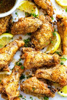 chicken wings with lemons and parsley on a white plate next to dipping sauce