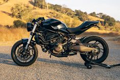 a black motorcycle parked on the side of a road next to a hill and grass