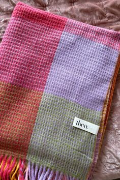 a pink, purple and green blanket with a tag on it sitting on a bed