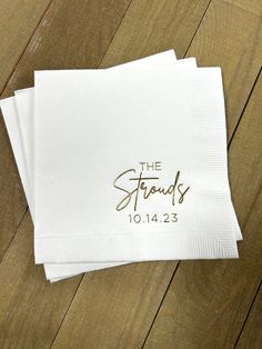 two personalized napkins with gold foil lettering on them sitting on a wooden surface