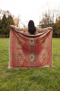 a woman is sitting in the grass with her back to the camera holding up a large rug