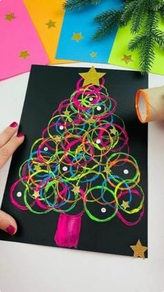 someone is making a christmas tree card with colored paper and scissors on the table next to it