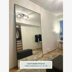 a large mirror in the middle of a room with clothes hanging on racks and a bench