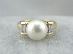 Simple and classic, this pearl ring features a beautifully polished yellow gold band with two sleek baguette diamonds set in each shoulder. Crafted of solid gold, this piece has a luxurious weight on the finger, and an understated, modernist design.  Material: 18K Yellow Gold Gem: Pearl Gem Measurements: 9.3 mm Round Accents: 2 Diamonds totaling of .56 Carats, G in Color, VVS in Clarity  Size of Ring: 7.50 Marks: "Hb18KP" Stamped on the inside band Sparkly Clothes, White Gold Diamond Earrings, Pearl Rings, Future Engagement Rings, Diamond Cocktail Ring, Modernist Design, Sparkly Things, Pearl Jewellery, Baguette Diamonds