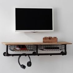 a tv mounted on the wall above two baskets with headphones hanging from it's hooks