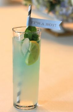 a tall glass filled with green and blue liquid next to a paper sign that says it's a boy