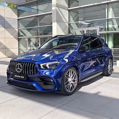 a blue mercedes suv is parked in front of a building with glass doors and windows