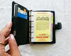 a hand holding an open wallet with a note book inside