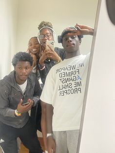 four people taking a selfie in front of a mirror with one person holding a cell phone