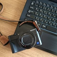 a camera sitting on top of a wooden table next to a laptop computer with a leather strap around it