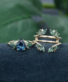 two rings with blue and green stones are on top of a black piece of cloth