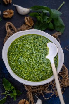 a white bowl filled with green pesto next to garlic and mushrooms on a blue surface