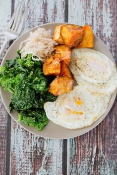 a white plate topped with eggs and potatoes next to green leafy salad on top of a wooden table