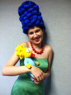 a woman with blue hair holding a stuffed animal in her arms and smiling at the camera