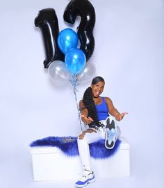 a woman sitting on top of a white box holding blue and black balloons in the air