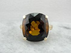 This simple, vintage cocktail mounting with only polished shoulders for decoration, is the perfect canvas for the amazing rich Dravite Tourmaline in the center. The deep, rich brown color is pierced by flickering colors when moved in the light! Dravite Tourmaline is a pleochroic stone, meaning that it reflects more than one color; and this stone dazzles with bright flashes of orange and yellow! Metal: 14K Yellow Gold Gem: Dravite Tourmaline 17.81 Carats Gem Measurements: 16.3 x 14.9 mm, Rectangl Formal Brown Gemstone Ring, Elegant Brown Rings For Formal Occasions, Classic Brown Gemstone Rings, Brown Jewelry With Prong Setting For Formal Occasions, Formal Brown Jewelry With Prong Setting, Antique Brown Rings For Formal Occasions, Formal Brown Rings With Polished Finish, Modern Brown Rings For Formal Occasions, Modern Brown Ring For Formal Occasions