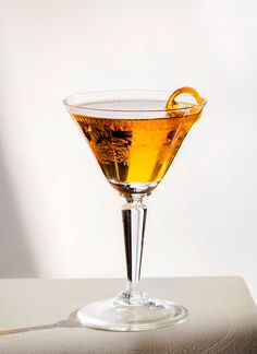 a glass filled with liquid and an orange peel on the rim, sitting on a table